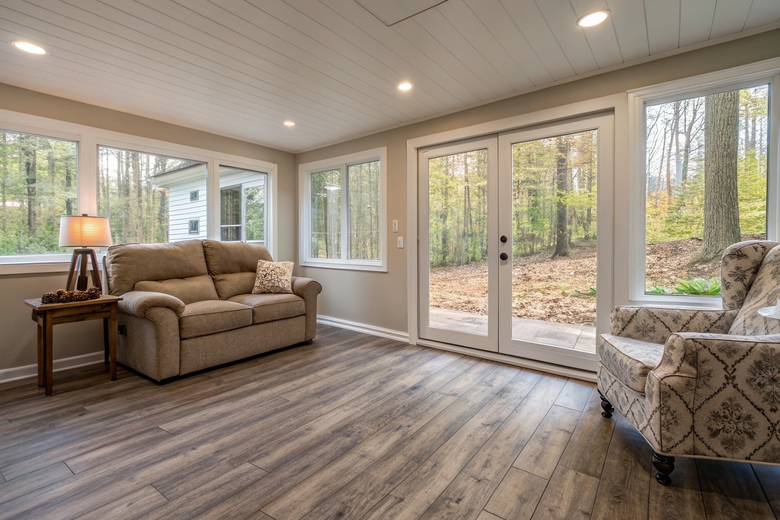 A bright, dry finished walkout basement with a sofa and glass doors to a wooded yard